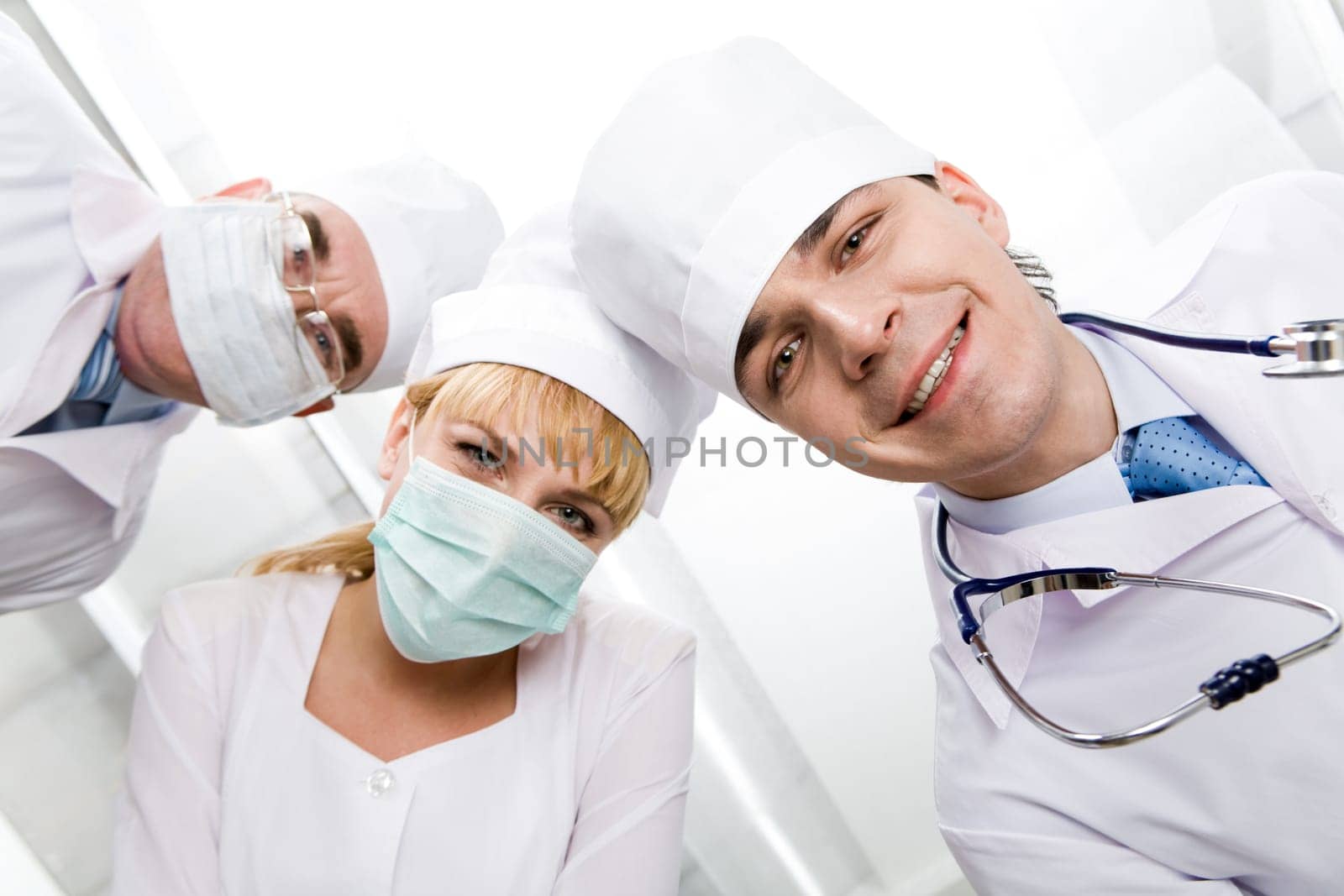 Below view of happy doctors with nurse between them looking at camera