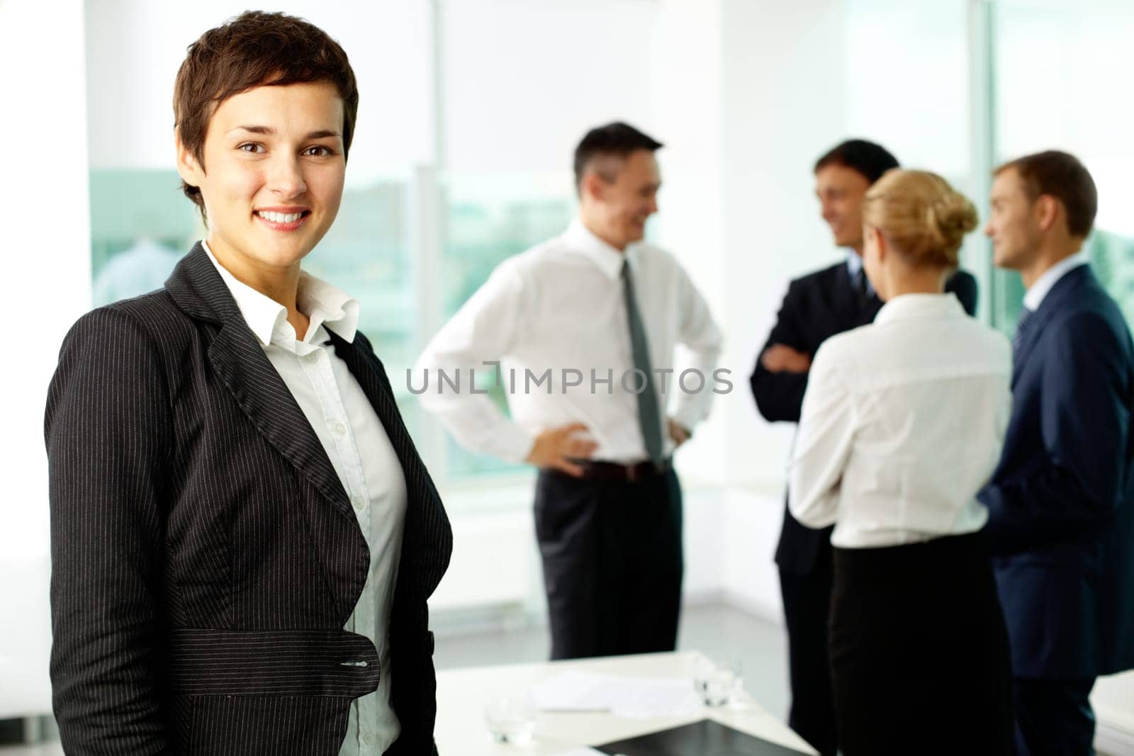 Attractive businesswoman looking at camera and smiling aginst her colleagues