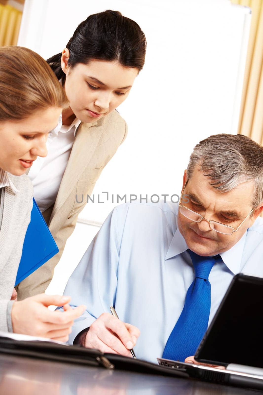 Image of serious businessman signing contract with two females near by