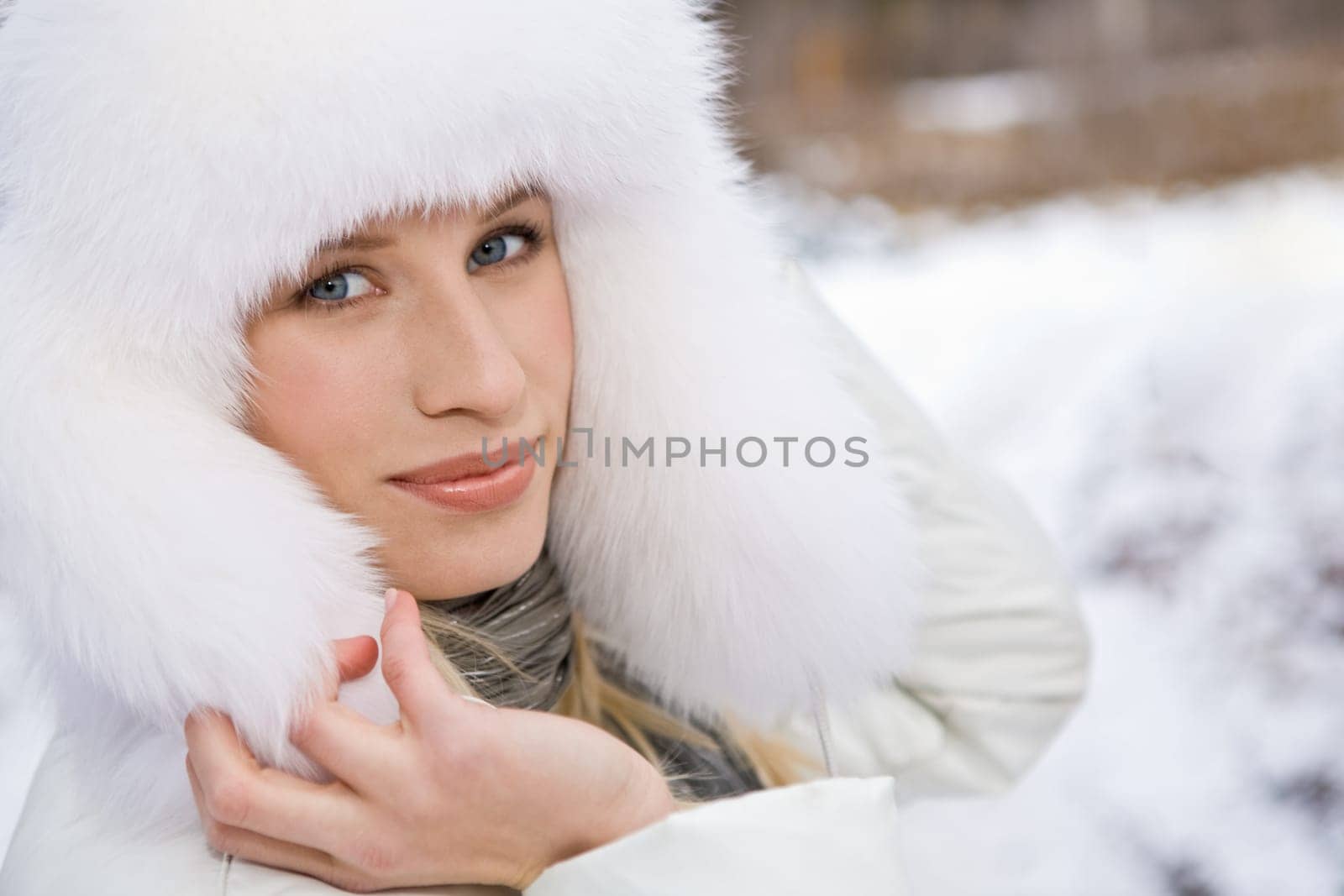 Pretty woman in white fur cap touching it and looking at camera
