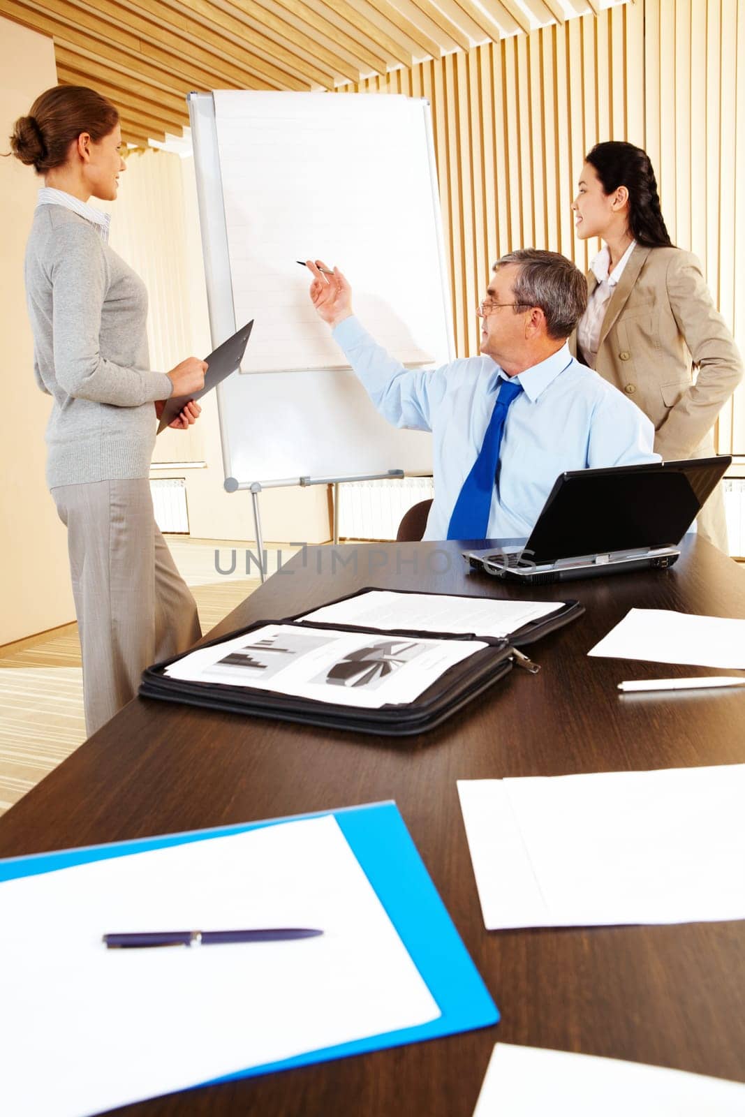 Photo of successful man pointing at whiteboard with two businesswomen standing near by
