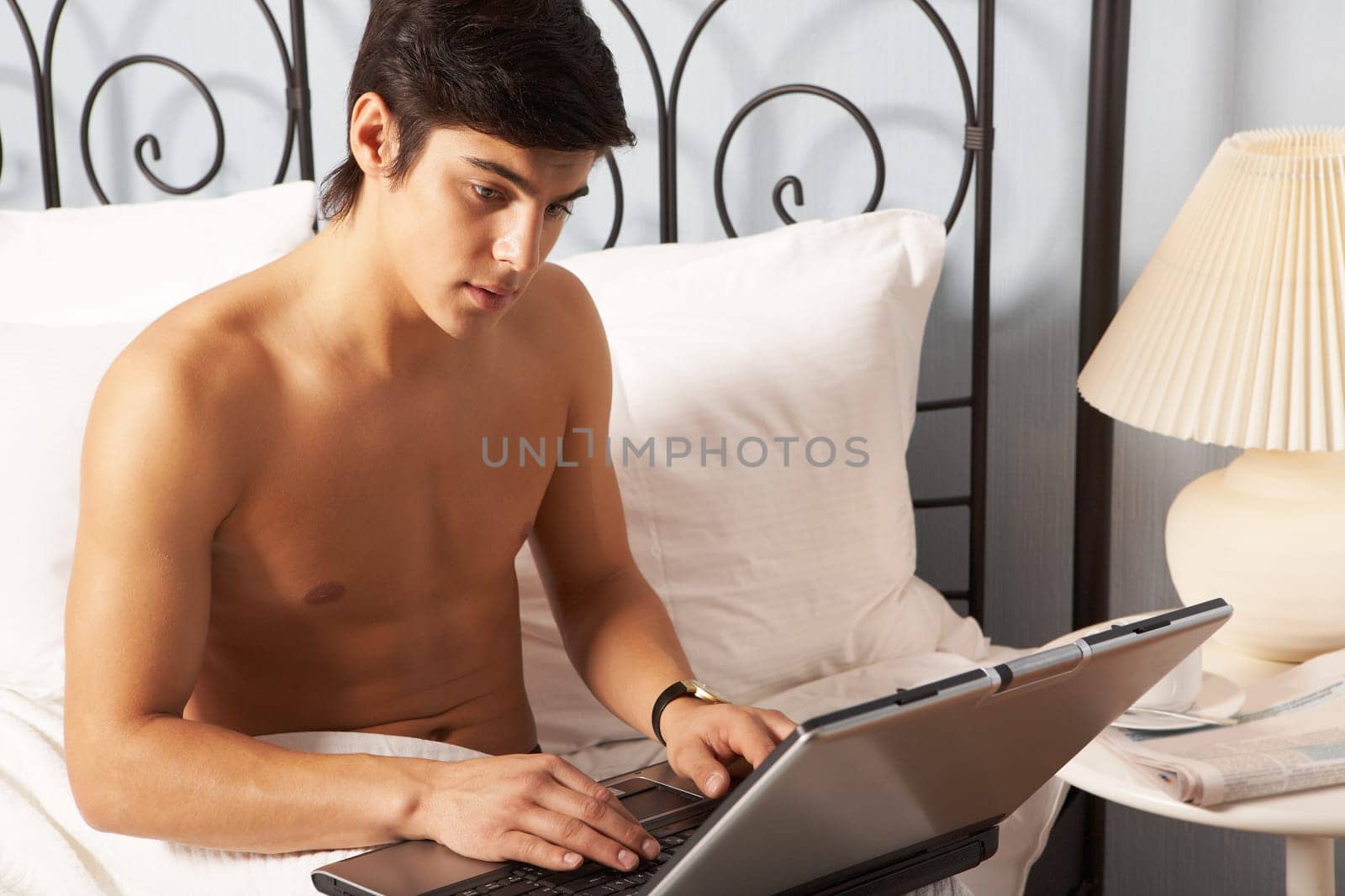 Young man sitting on bed and typing on laptop