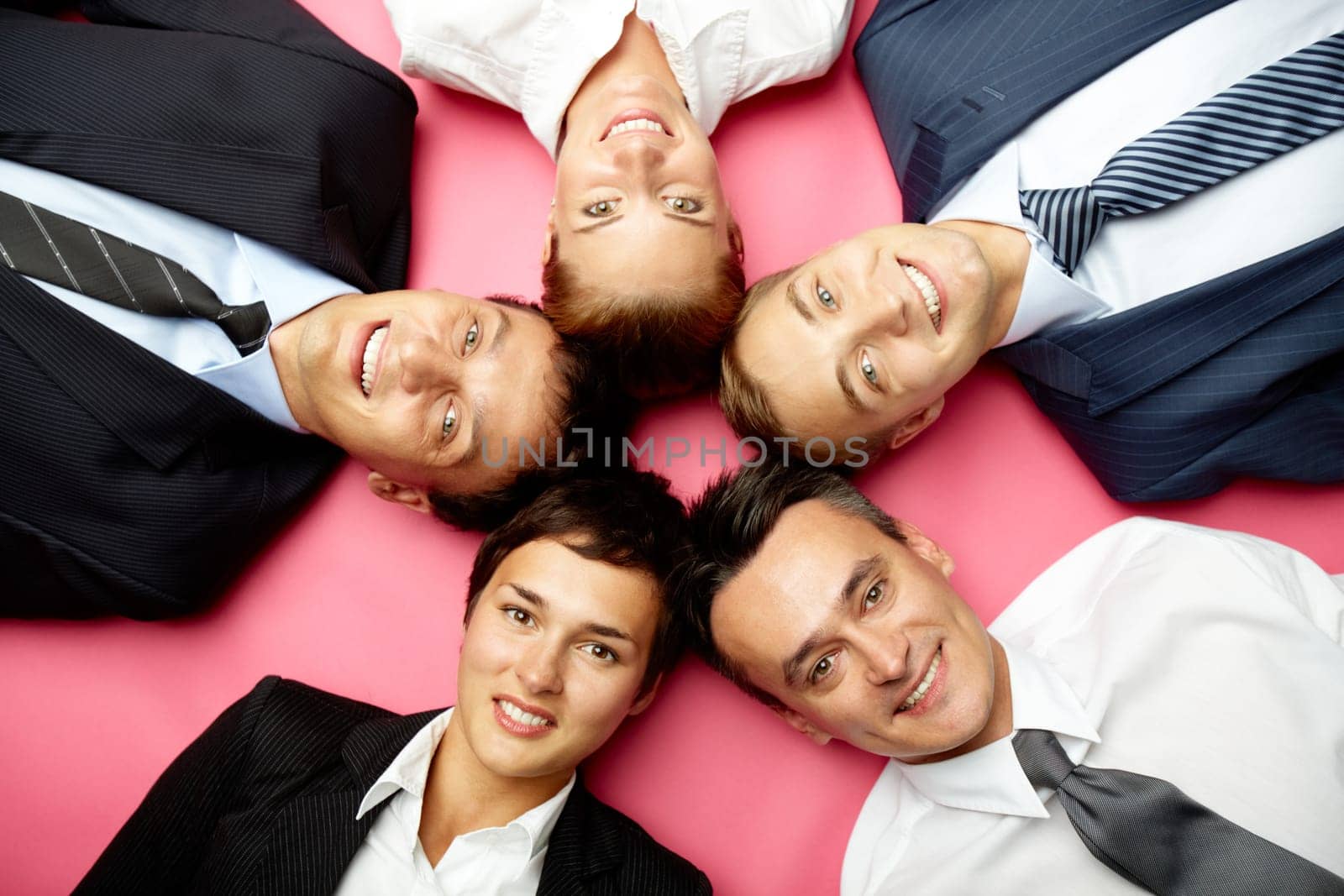 Five businesspeople lying in circle, looking at camera and smiling