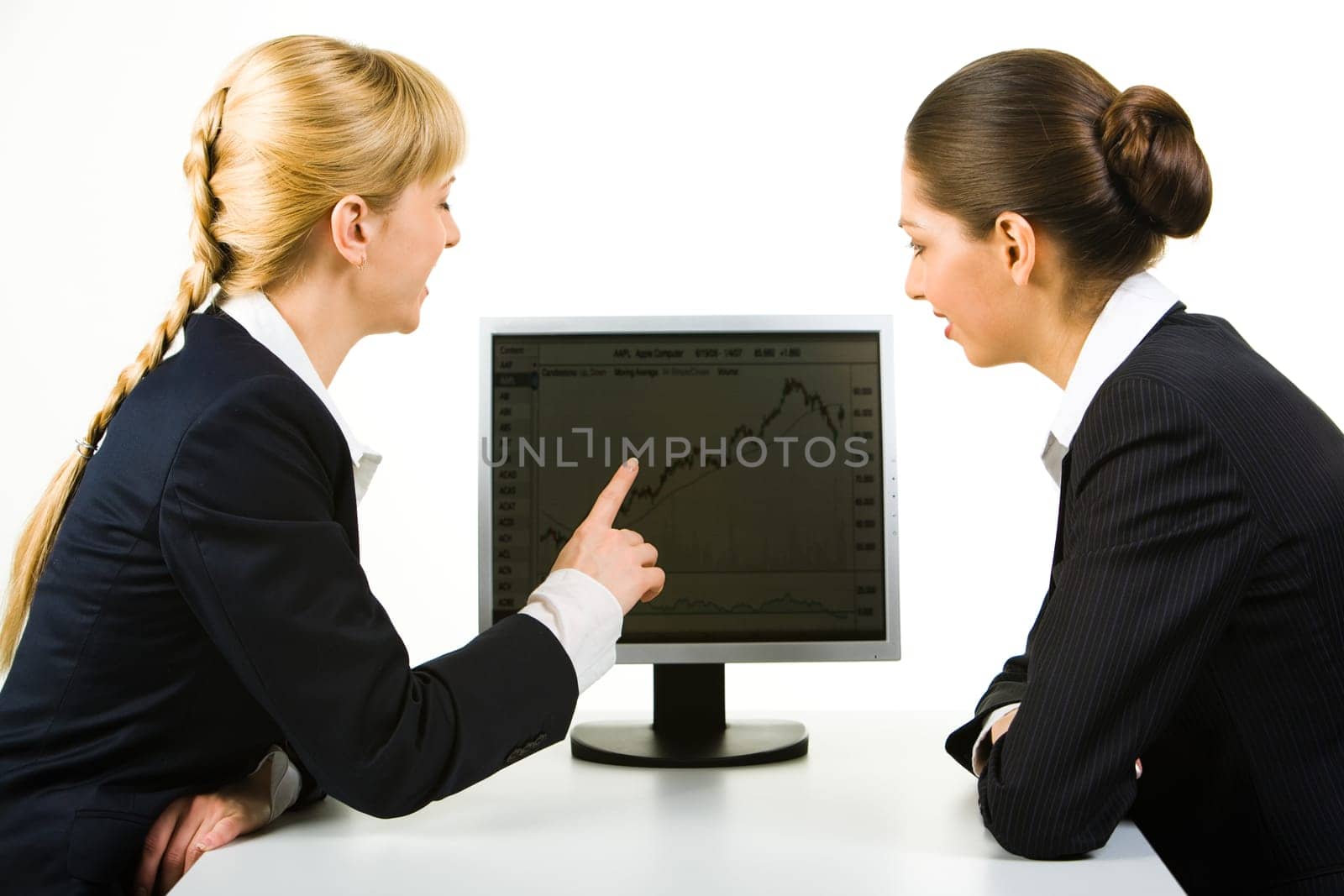 Portrait of two businesswomen sitting near computer while one of them pointing at its monitor