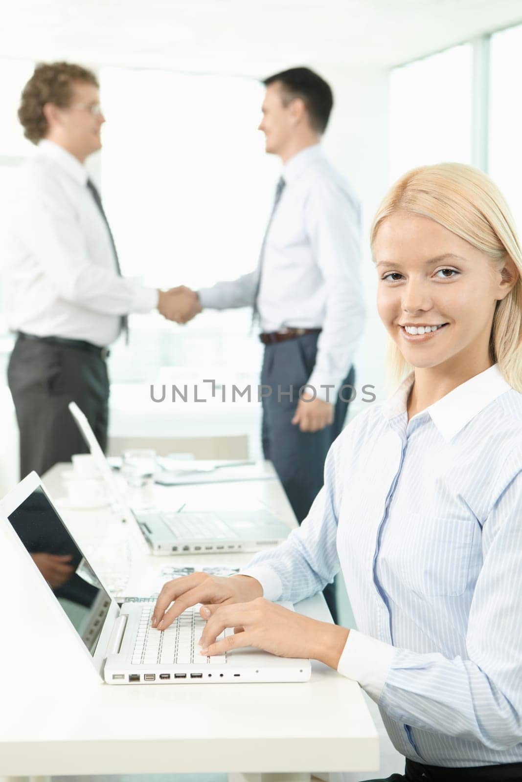 A beautiful businesswoman looking at camera with handshaking men on background