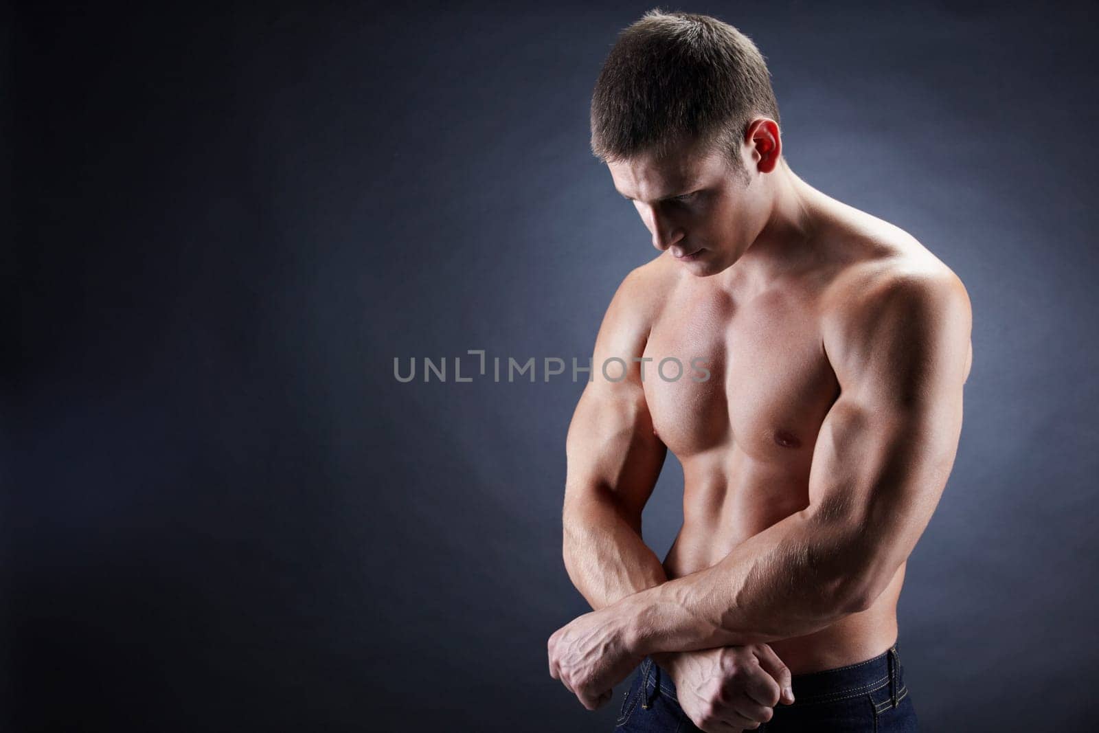 Image of shirtless man looking downwards with his arms crossed by stomach