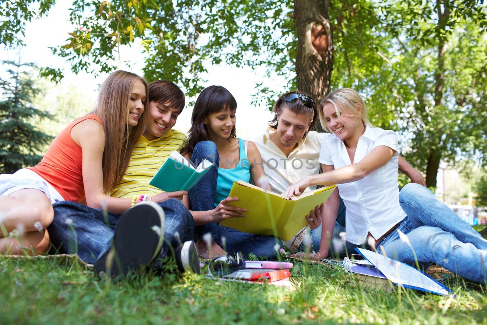Portrait of cheerful students talking and reading books in park together