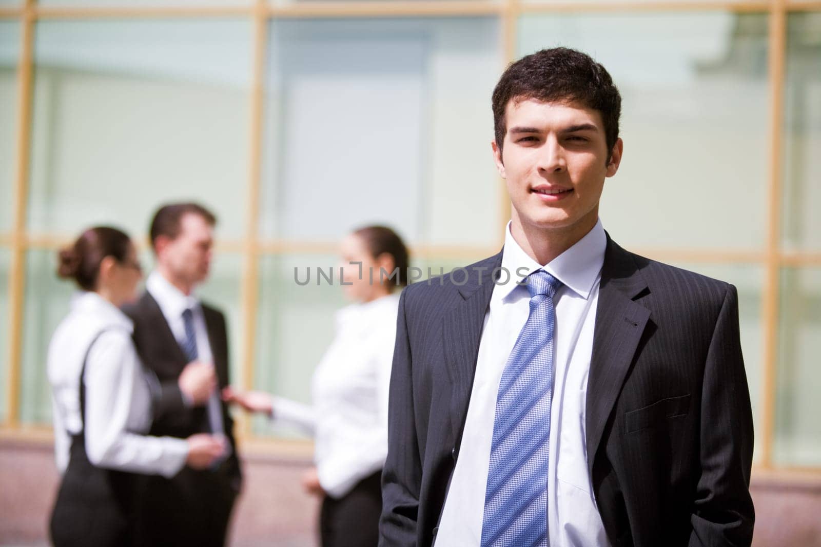 Portrait of handsome employer smiling at camera with consulting staff on background