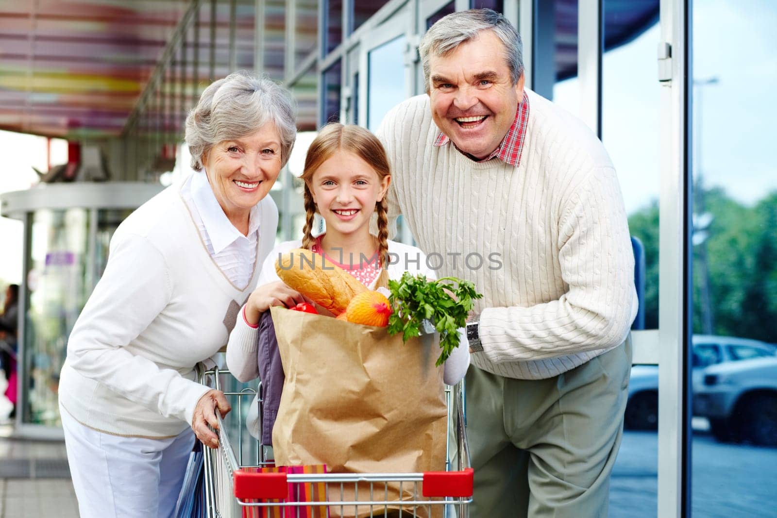 Portrait of happy grandparents and granddaughter near supermarket