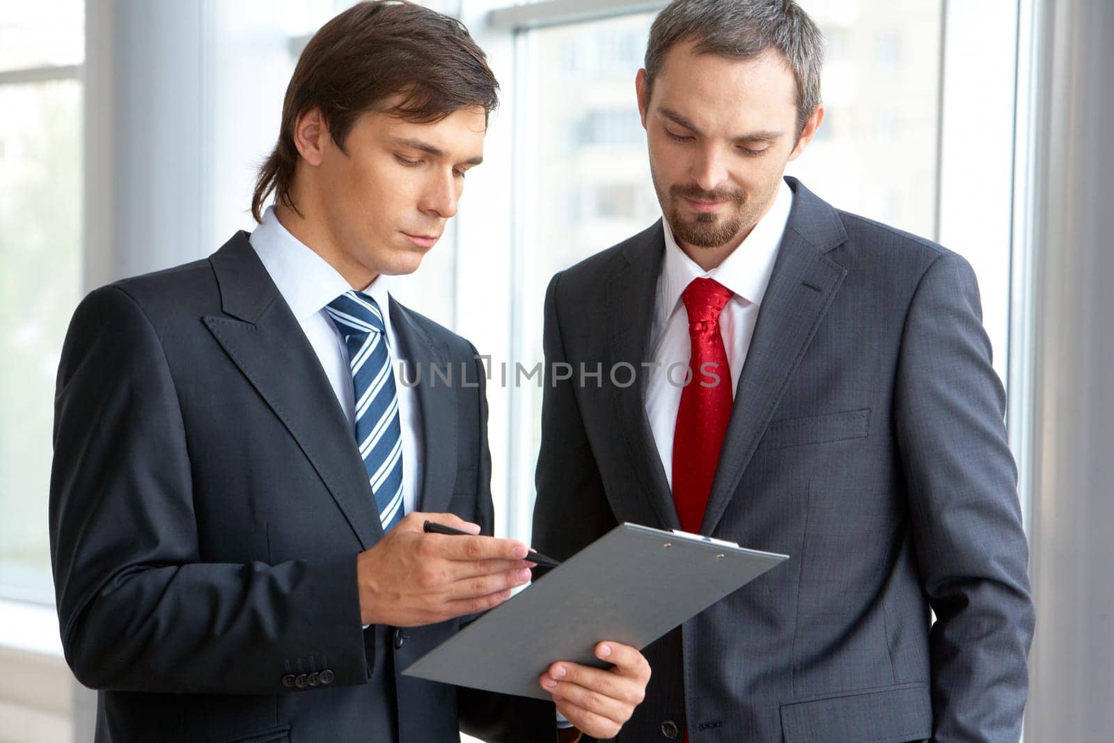 Image of confident businessman looking at document in partners hand while discussing it