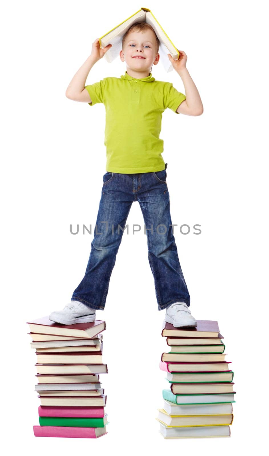 A cheerful boy standing on two heaps of books and holding a book over his head