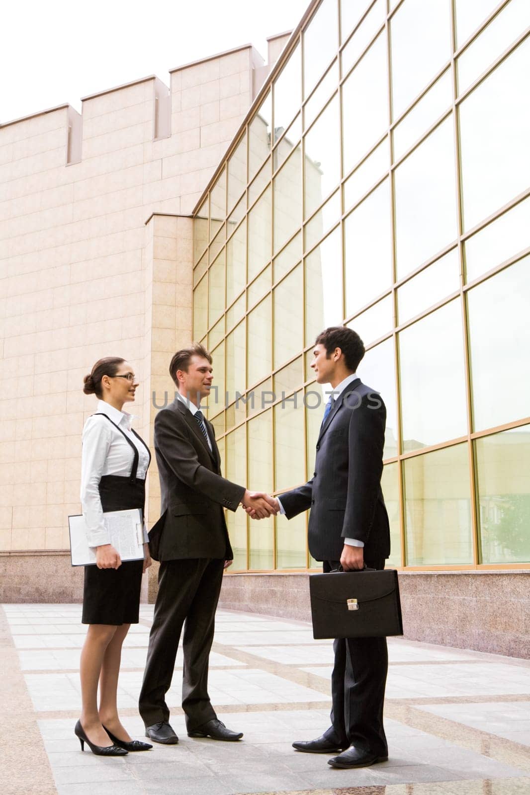 Portrait of two businessmen shaking hands after signing contract with pretty employee standing near by