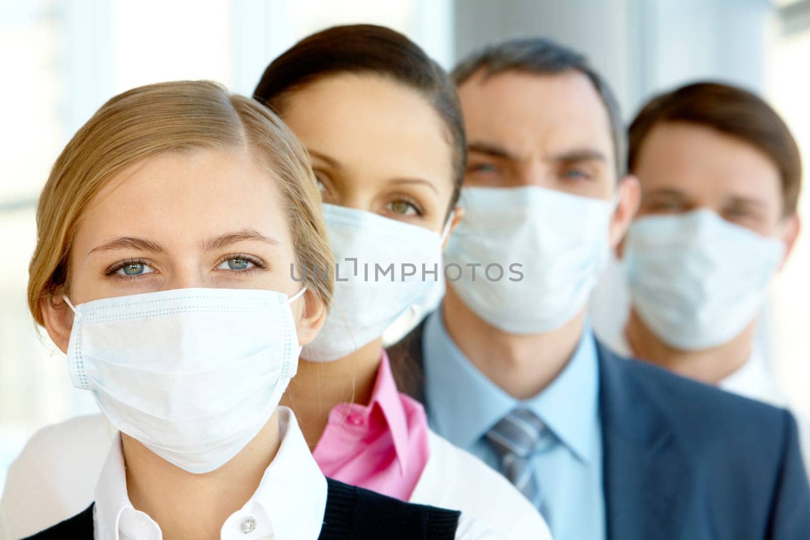 Pretty female in protective mask looking at camera with row of partners behind
