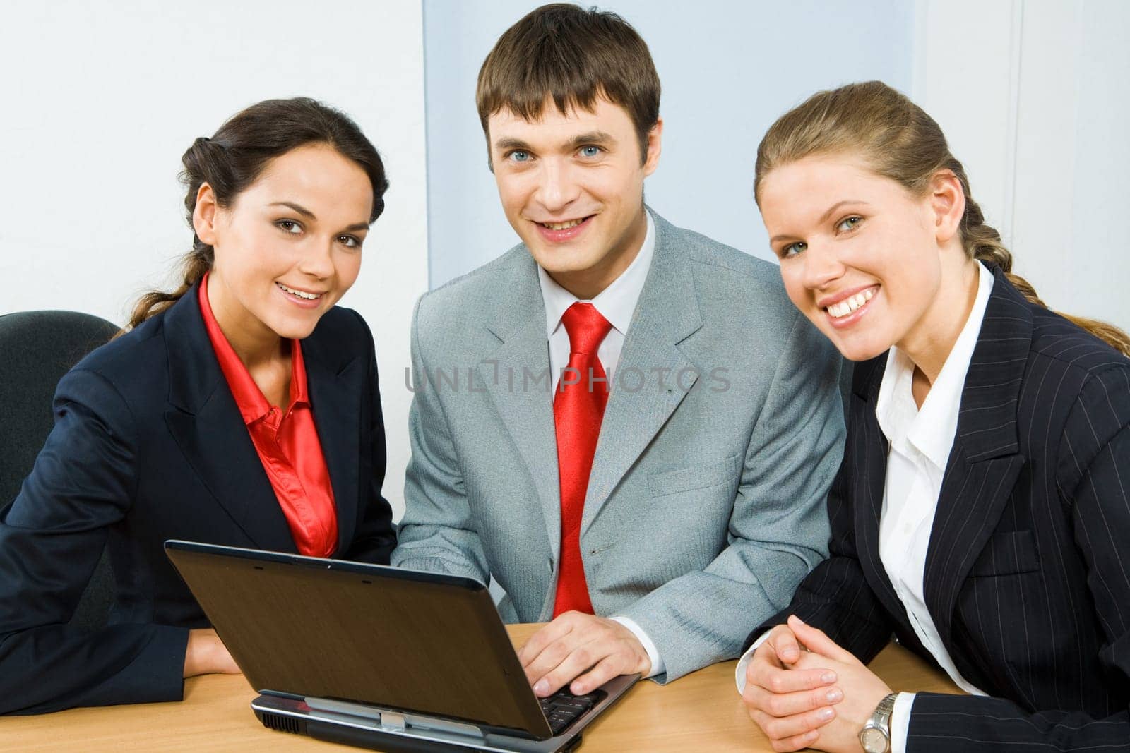 Group of three business people sitting at the table and looking at camera