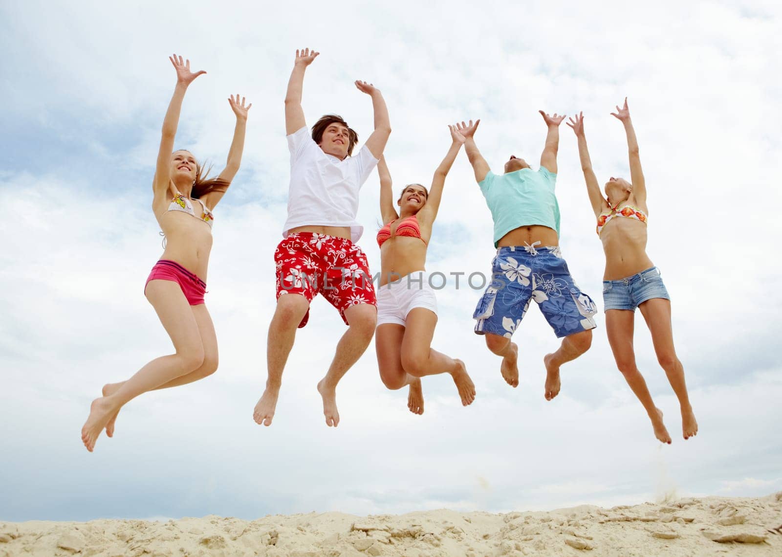 Photo of five friends in high jump over sandy beach