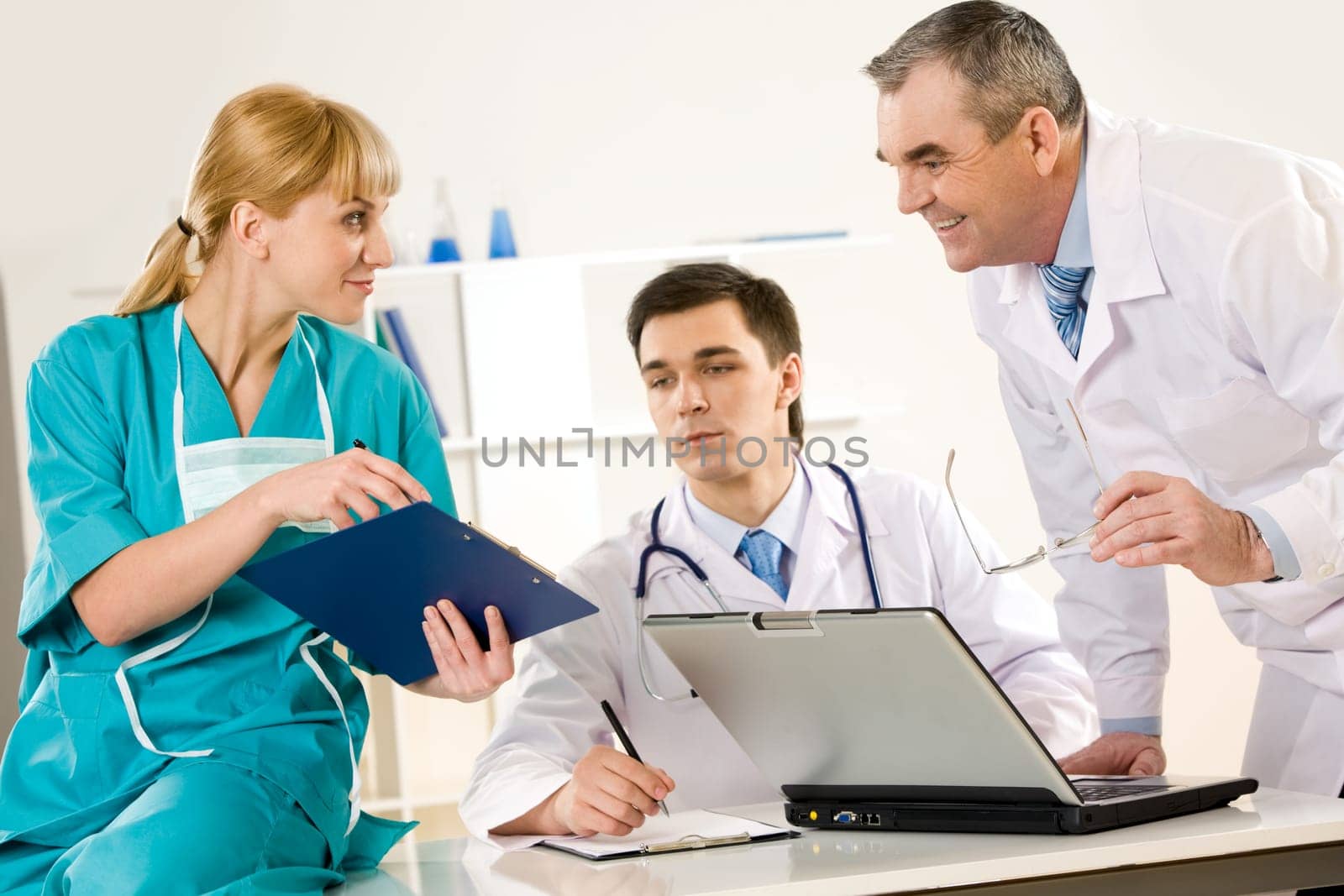 Photo of aged physician and young clinician looking at document in nurses hand