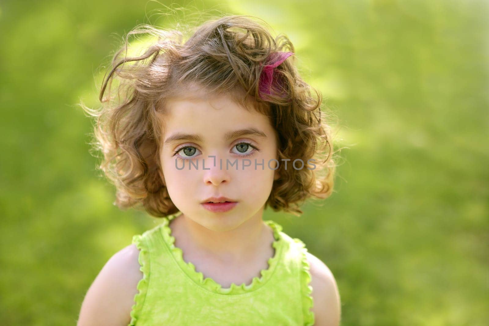 Beautiful brunette blue eyes little girl portrait on the park green grass