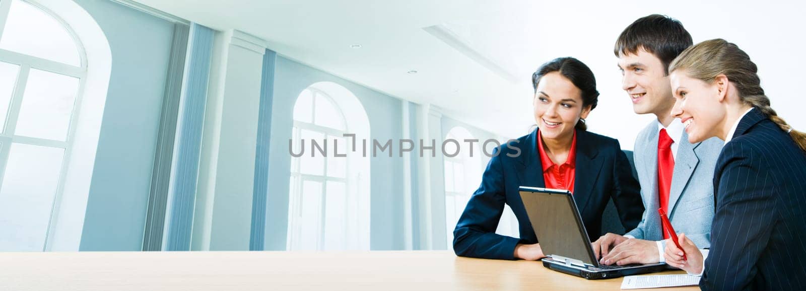 Photo of three office workers sitting at the table on the background of office building
