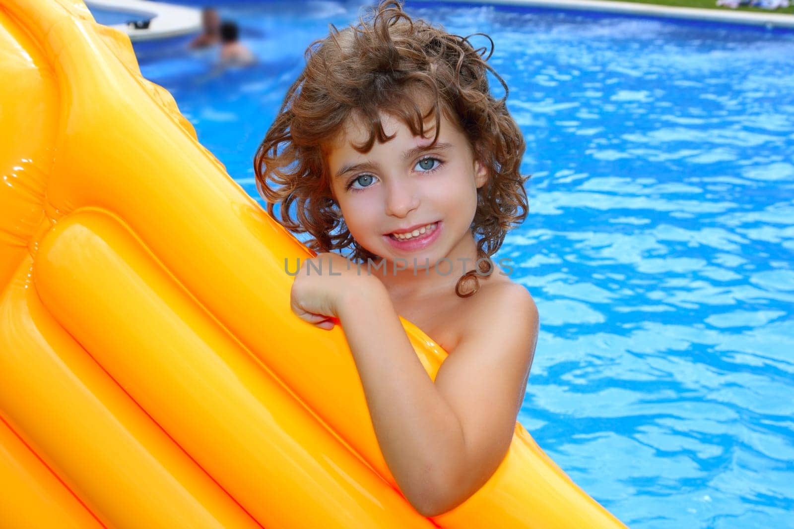 Beautiful little girl holding yellow pool float smiling over blue water