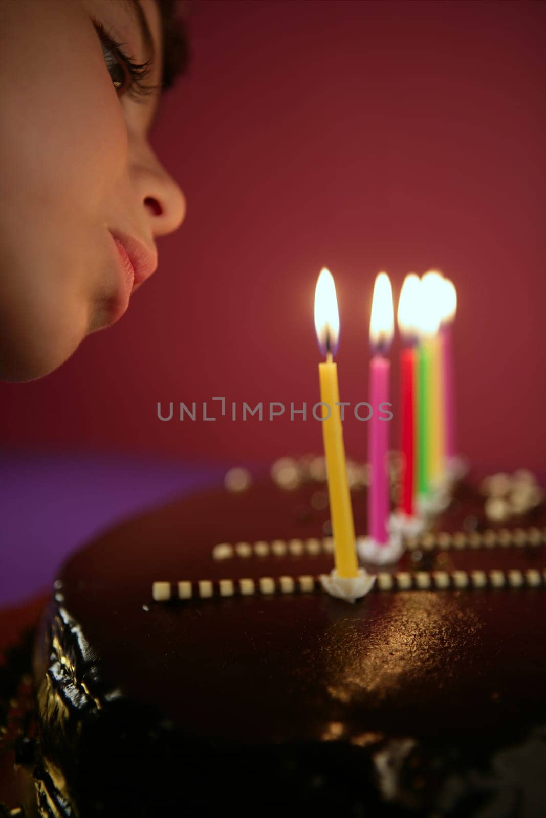 Little girl blowing birthday chocolate cake candles in a row over red background