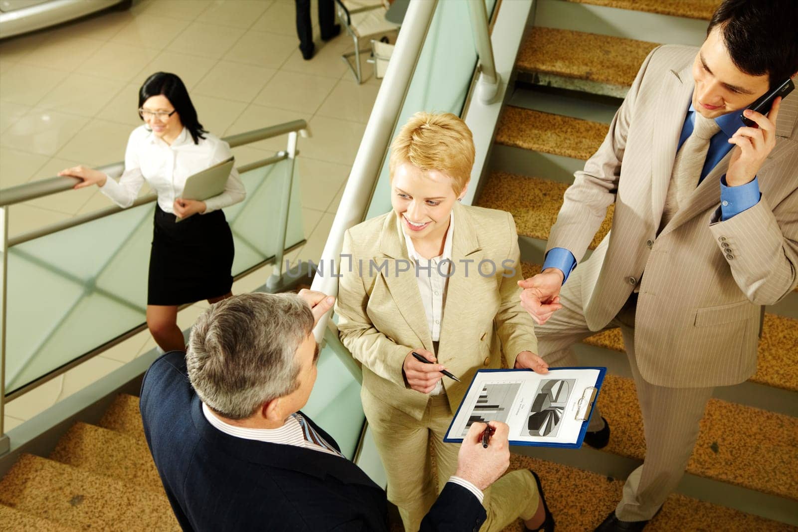 Photo of busy partners discussing papers while on stairs of office building