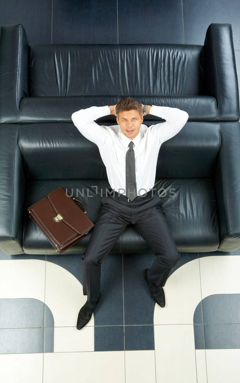 Portrait of businessman touching head while sitting on sofa and looking at camera