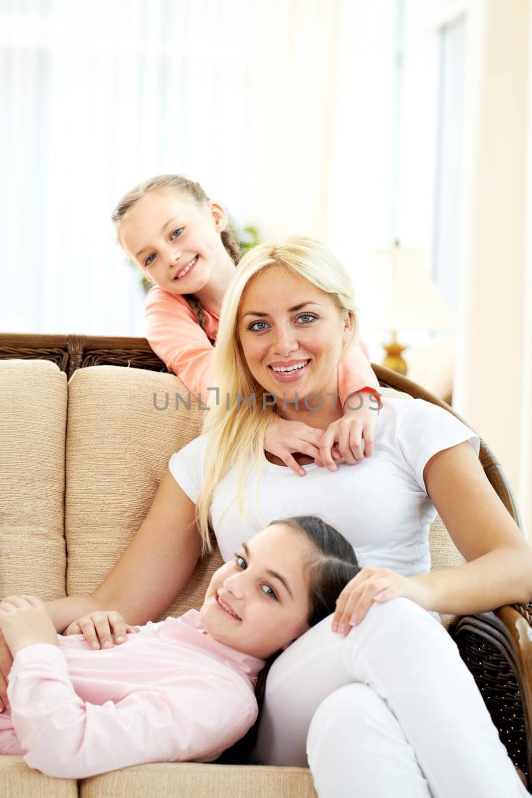 Portrait of happy woman and two daughters sitting on sofa and looking at camera