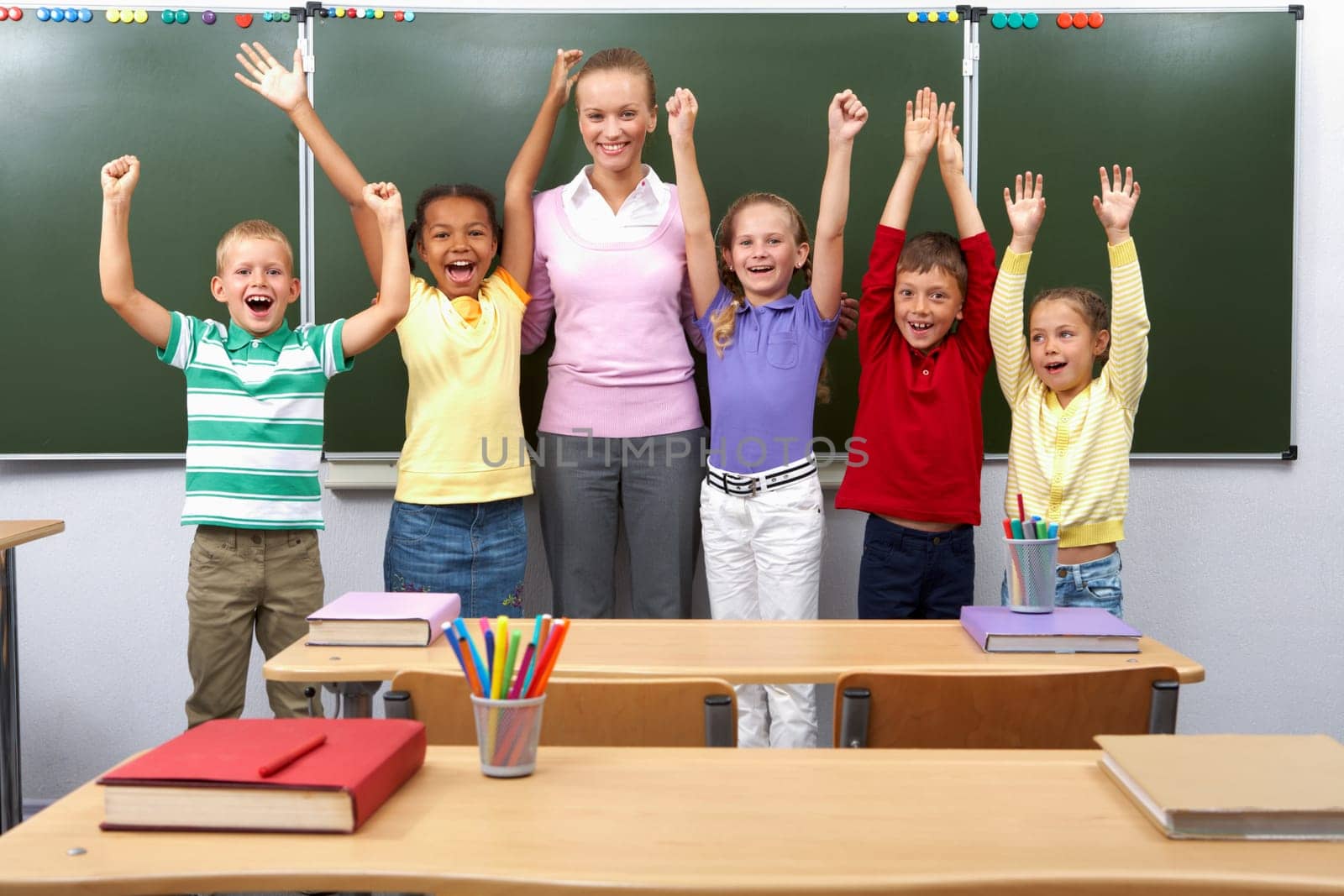 Line of cute schoolchildren raising arms with their teacher in the middle