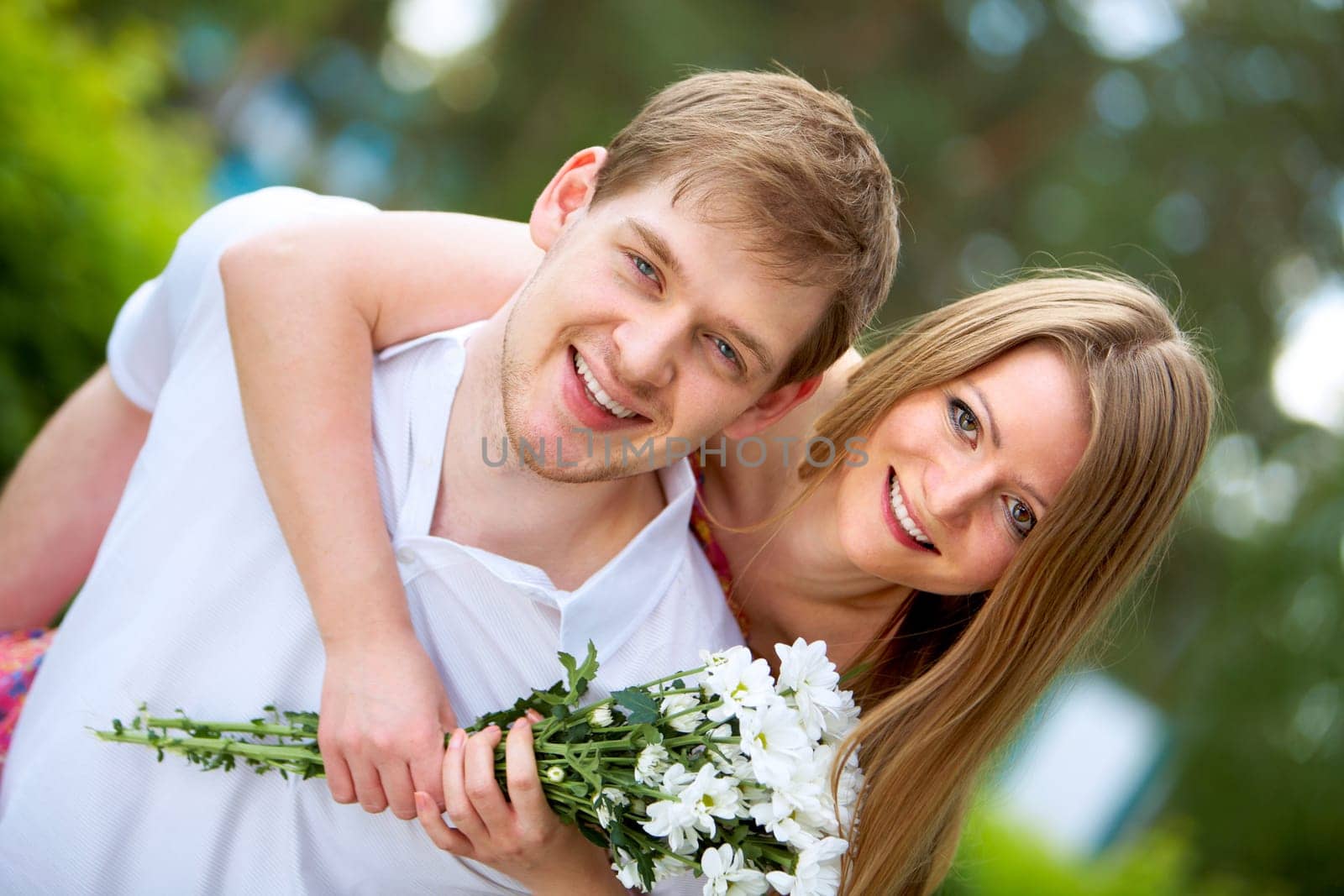 Photo of happy girl with bunch of white chrysanthemums embracing handsome male