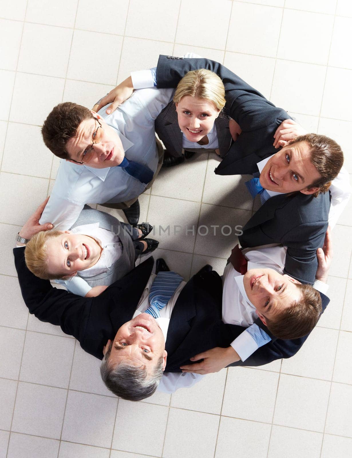 Above view of several business partners looking upwards at camera while embracing each other