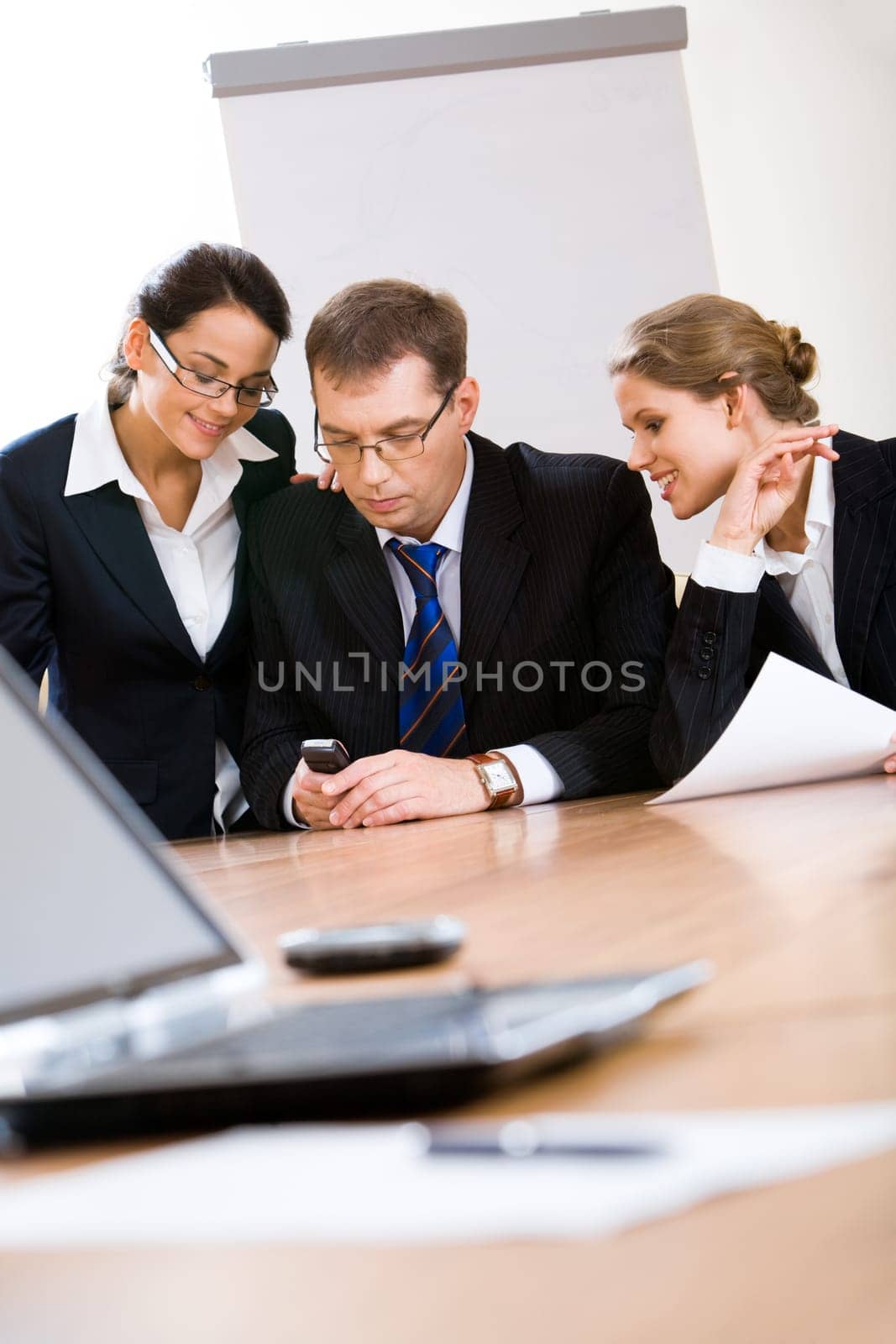 Three employees look at phone which the man holds at meeting
