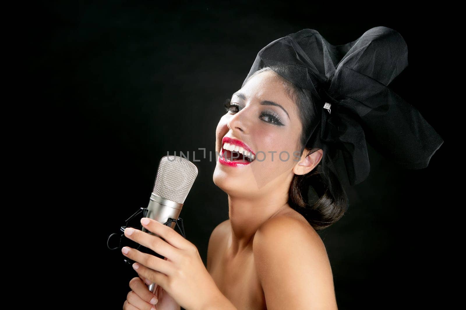 Beautiful woman singing on a vintage microphone on black background