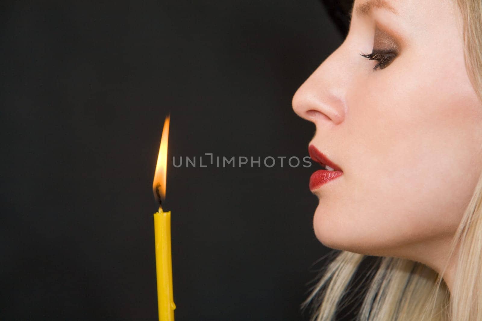 Image of witch looking at burning candle on black background