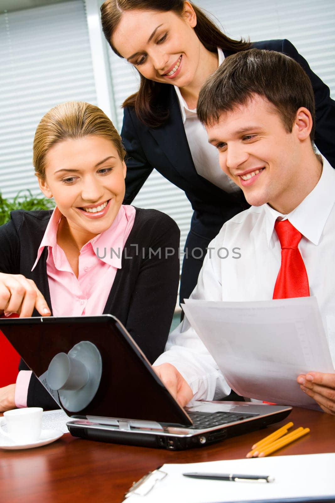 Vertical photo of a businessman looking at the screen of laptop with two businesswomen near by