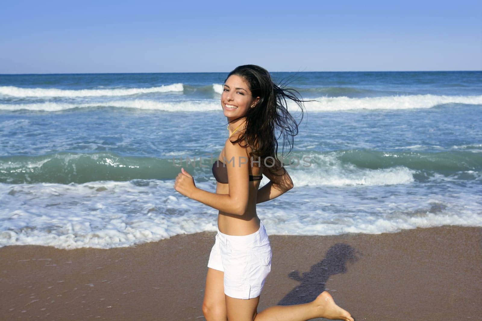 Beautiful summer brunette girl jumping on the blue beach