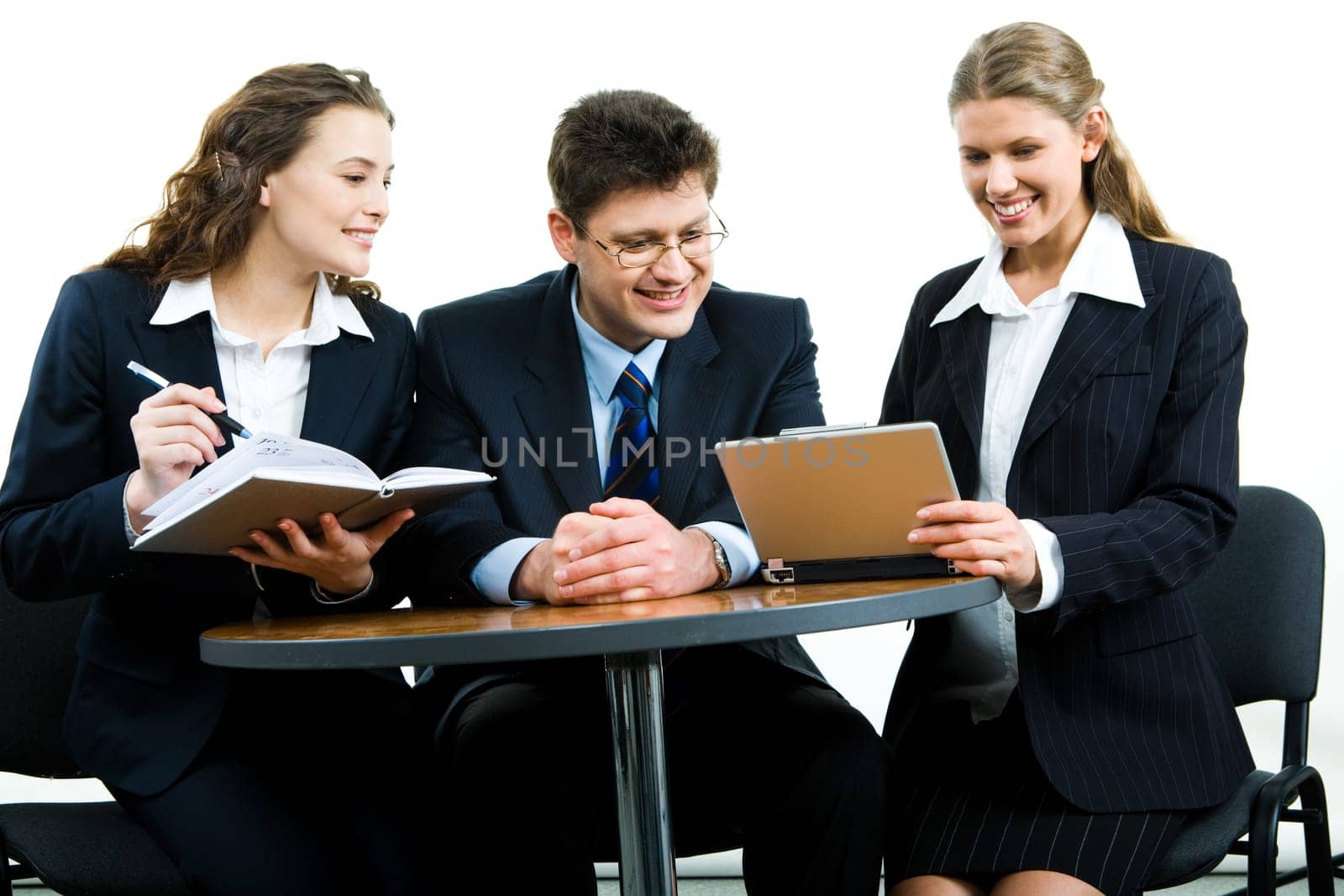 Photo of smiling young colleagues sitting next to each other at meeting and looking at the laptop screen together