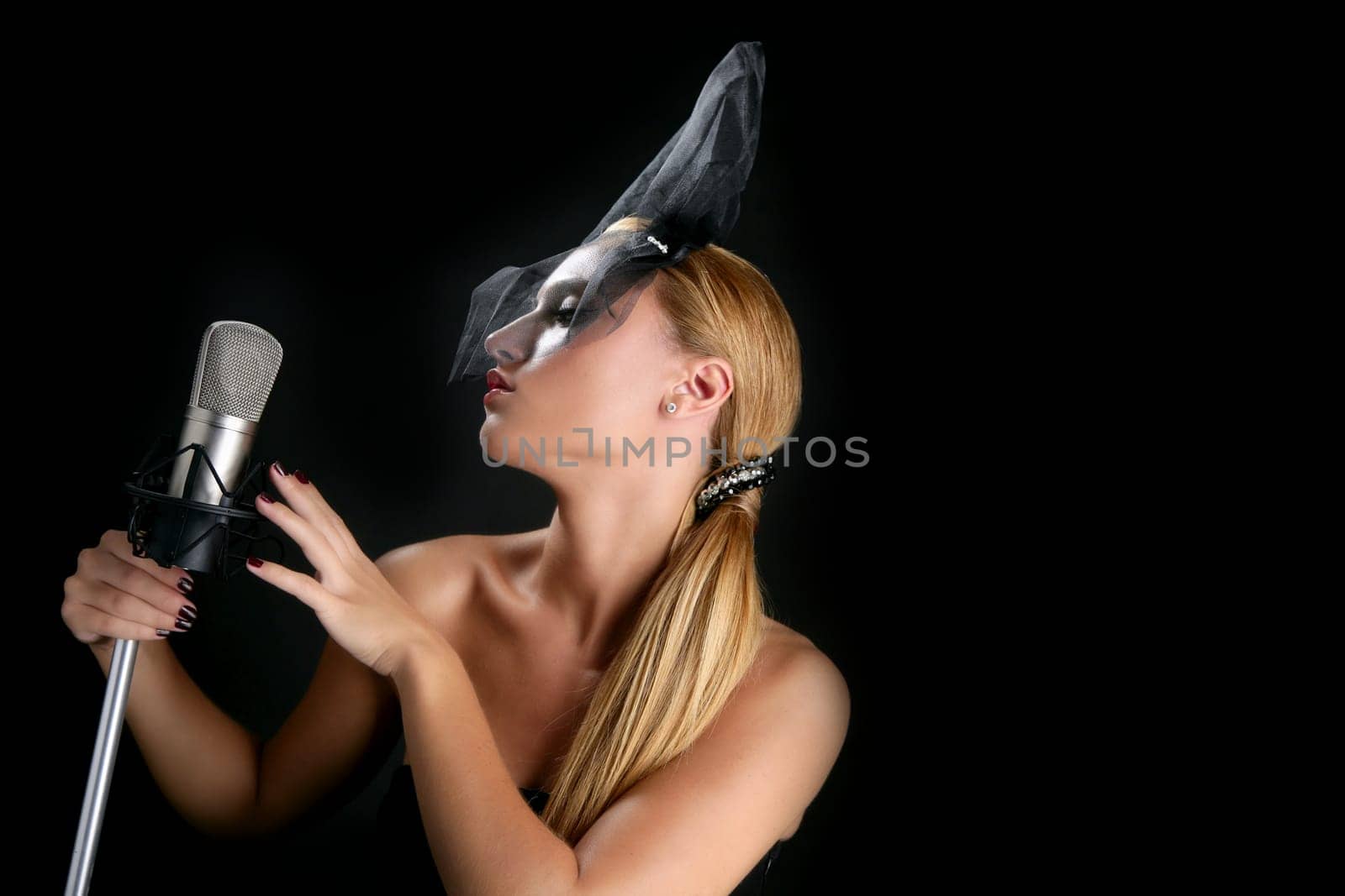 Beautiful woman singing on a vintage microphone on black background