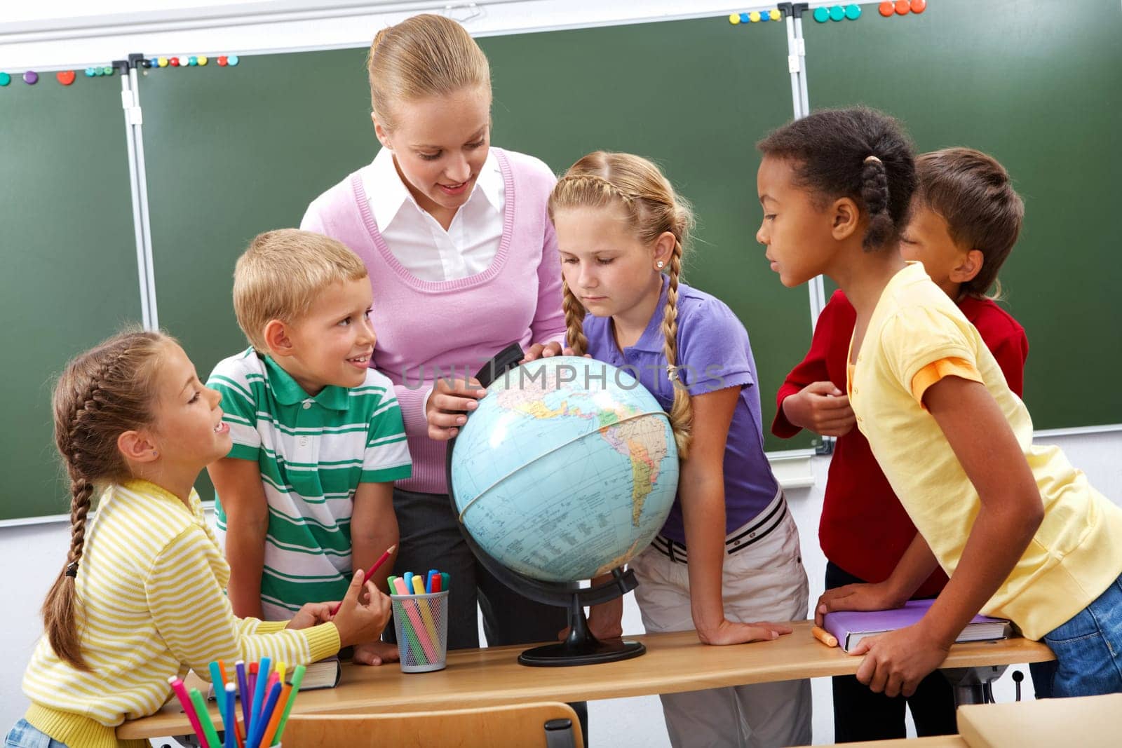Portrait of pupils looking at globe while listening to teacher during geography lesson