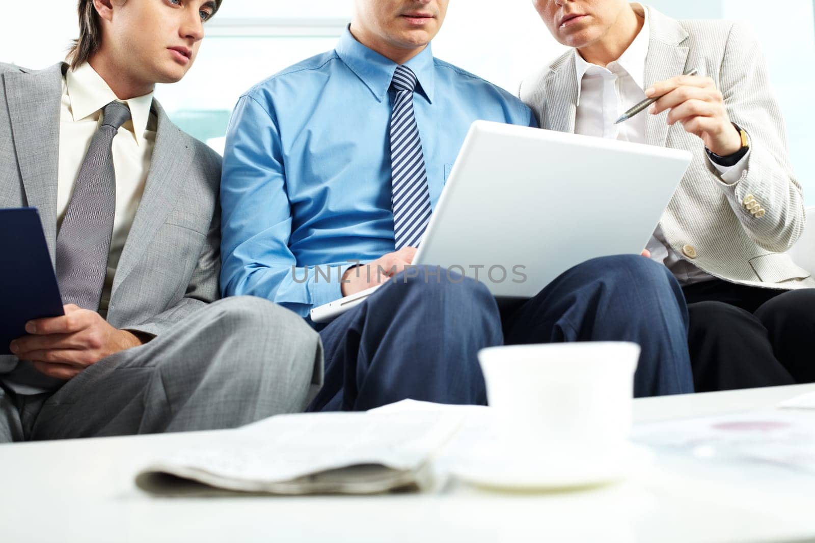 Three business people sitting on sofa and looking at laptop