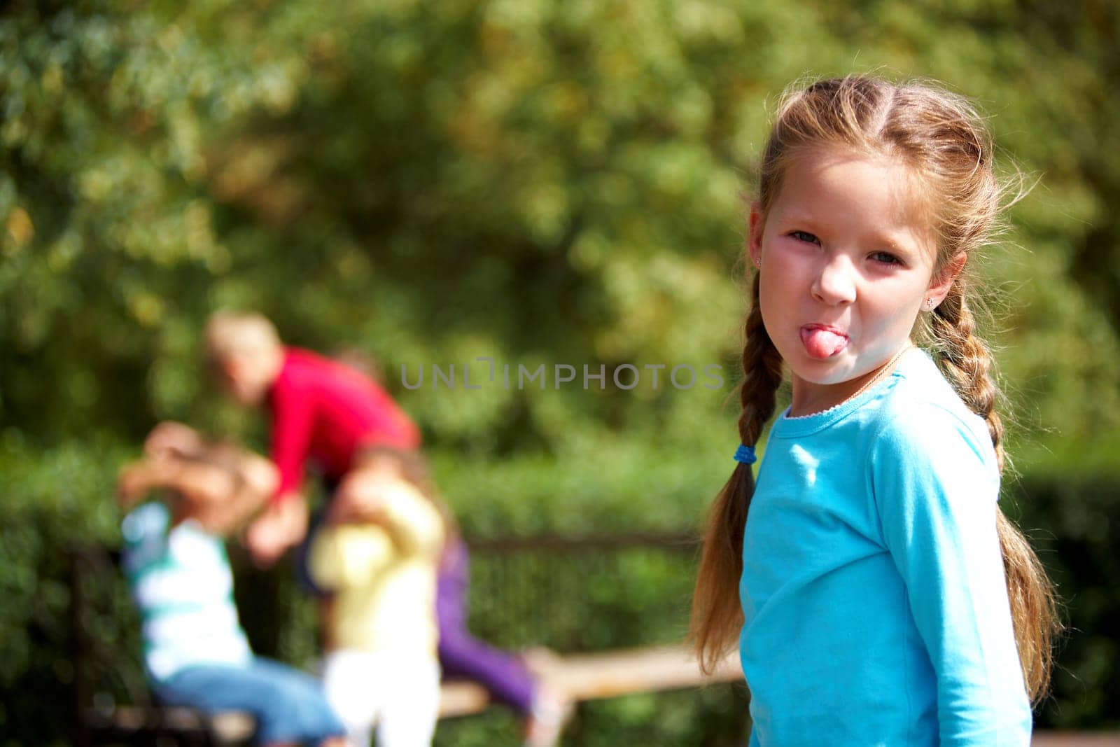 Portrait of funny girl looking at camera and showing tongue with her friends on background