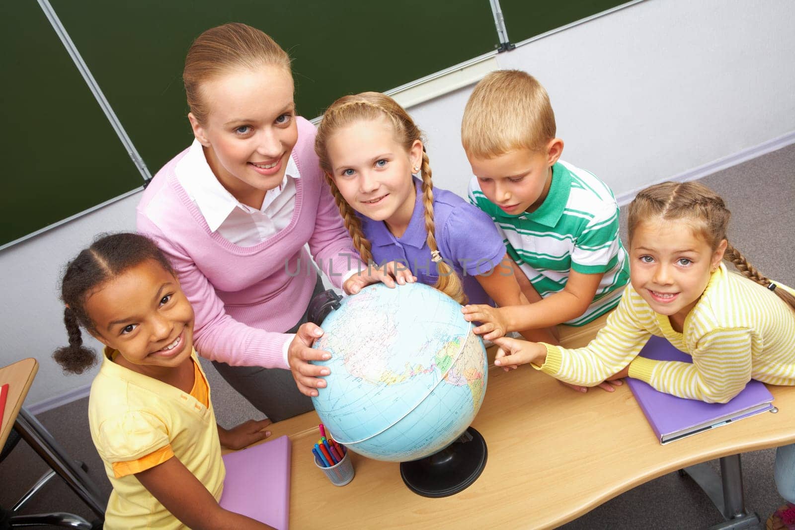Portrait of pupils and teacher looking at camera with globe on table during geography lesson