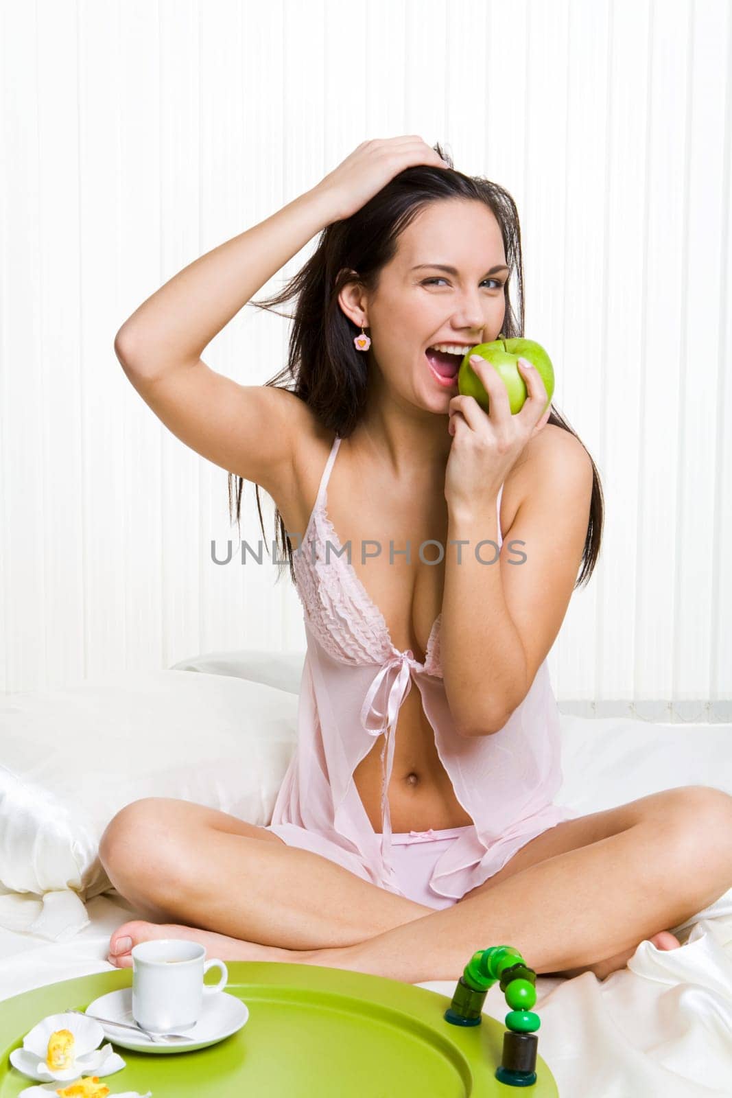 Portrait of healthy woman sitting on bed and eating fresh green apple