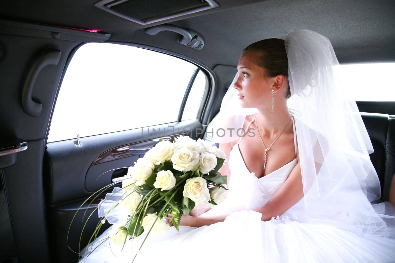 Portrait of beautiful bride with rose bouquet in hands sitting in the car and looking aside