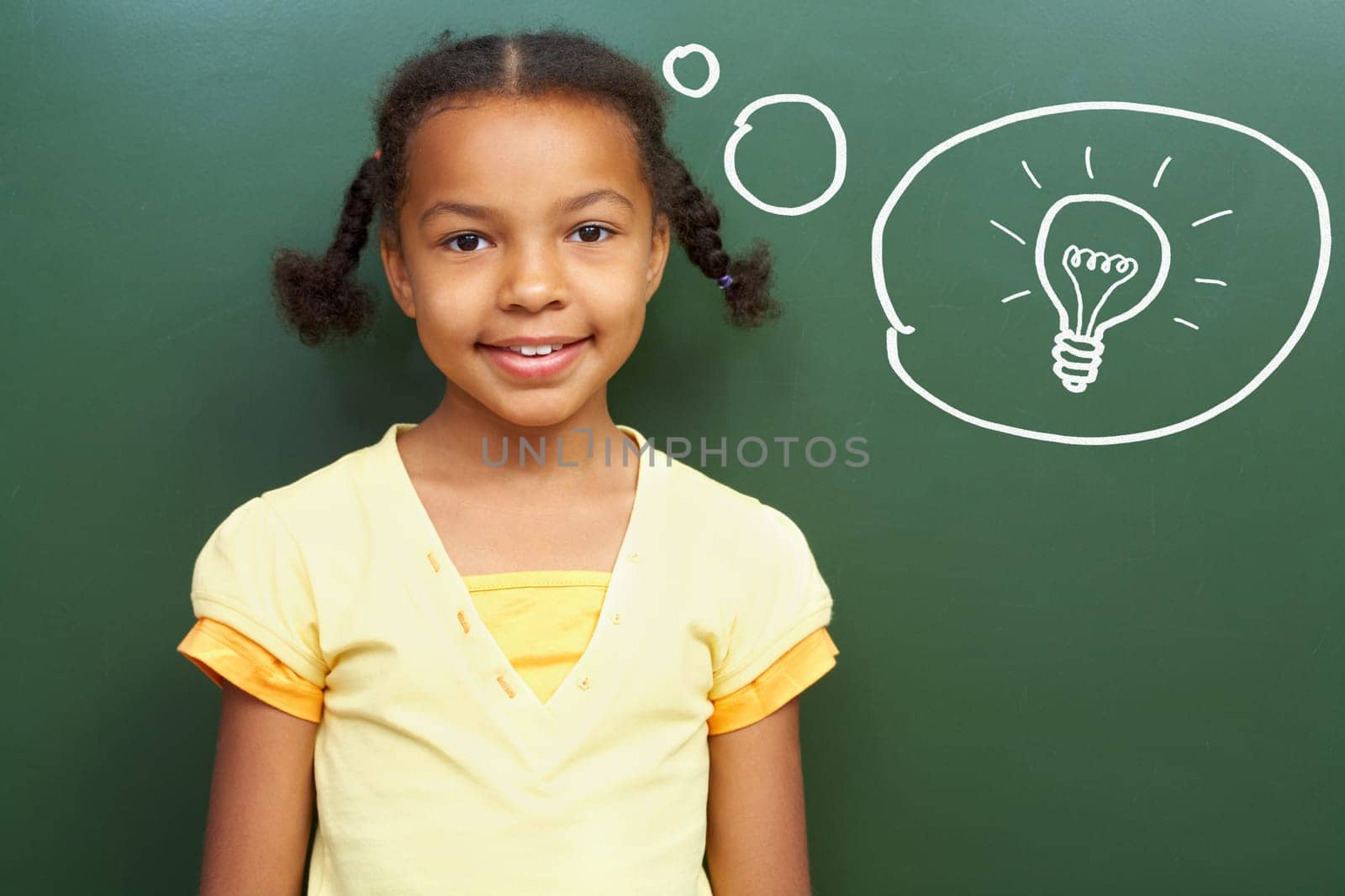 Portrait of smart girl by the blackboard thinking of light idea and looking at camera