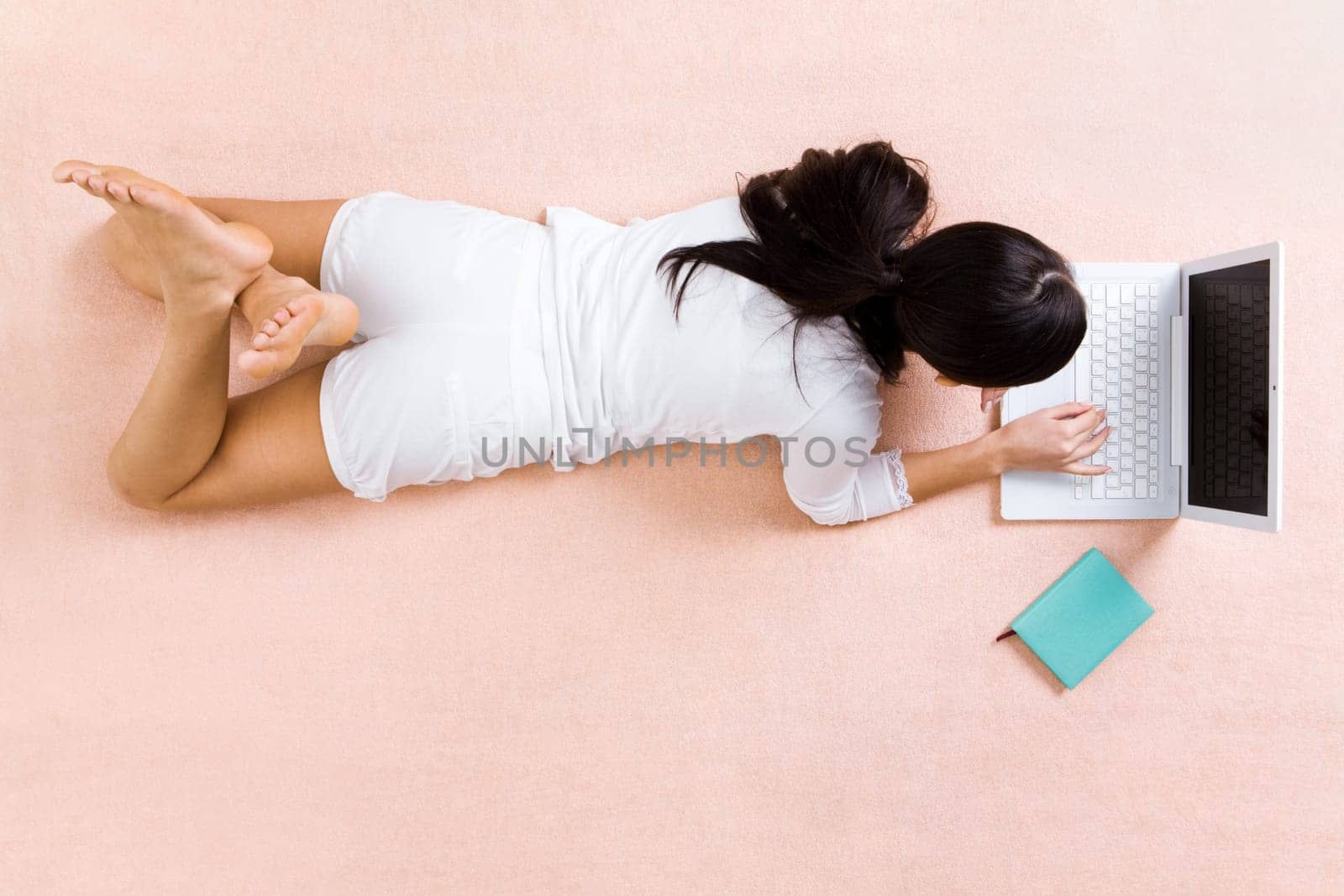 View from above of girl lying on bed and typing on laptop
