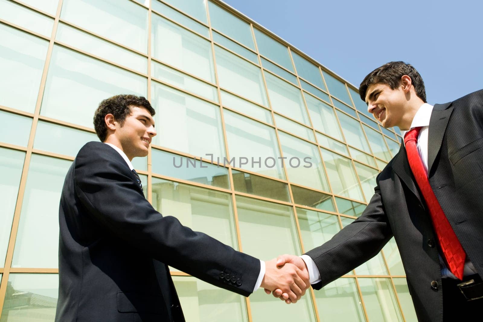 Photo of successful men handshaking at background of modern building