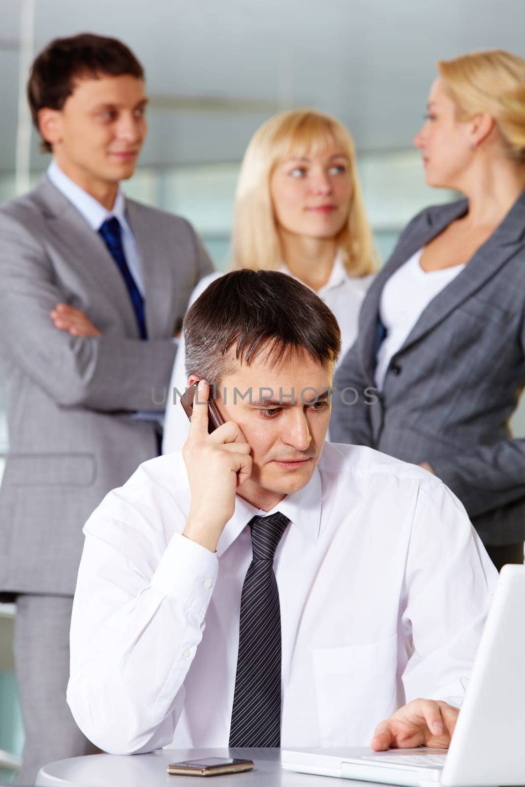 Portrait of businessman phoning and working with laptop on background of his partners
