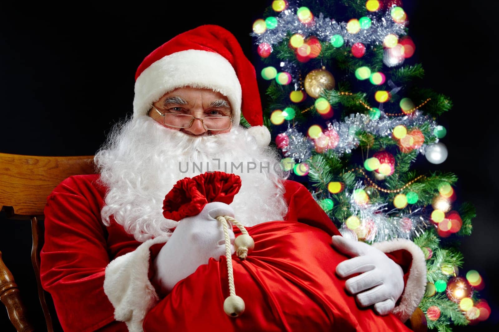 Santa sitting with a sack at the Christmas tree
