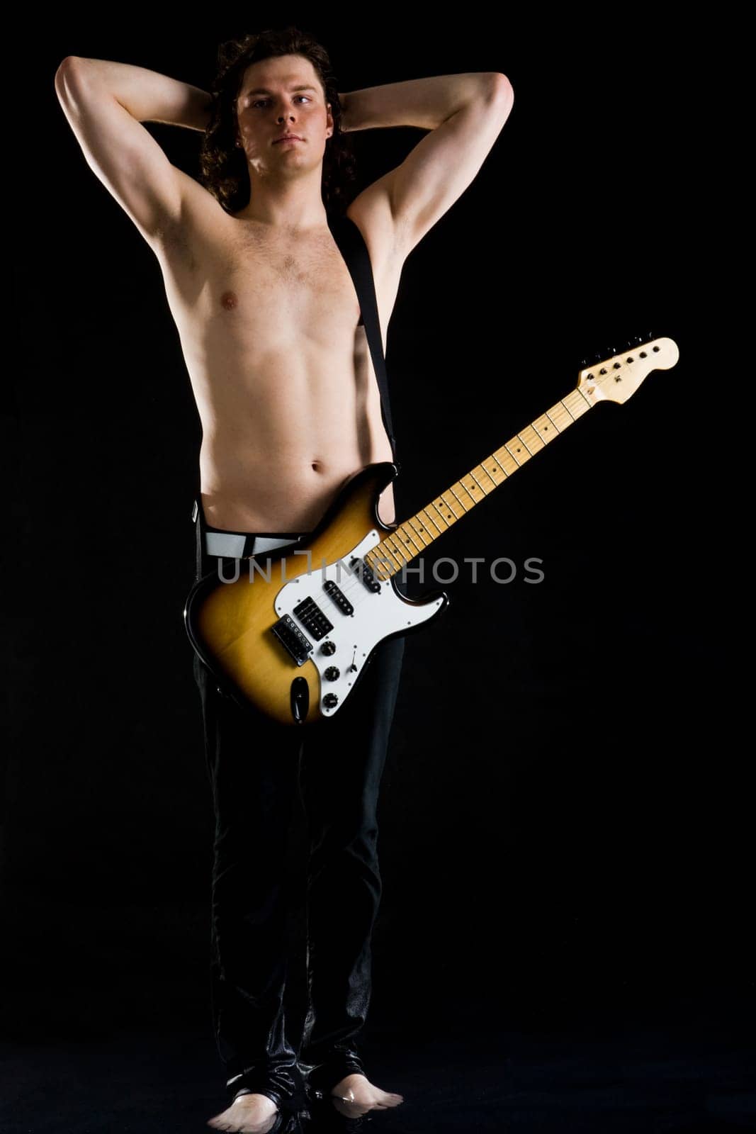 Portrait of young performer with bare torso and guitar standing in water