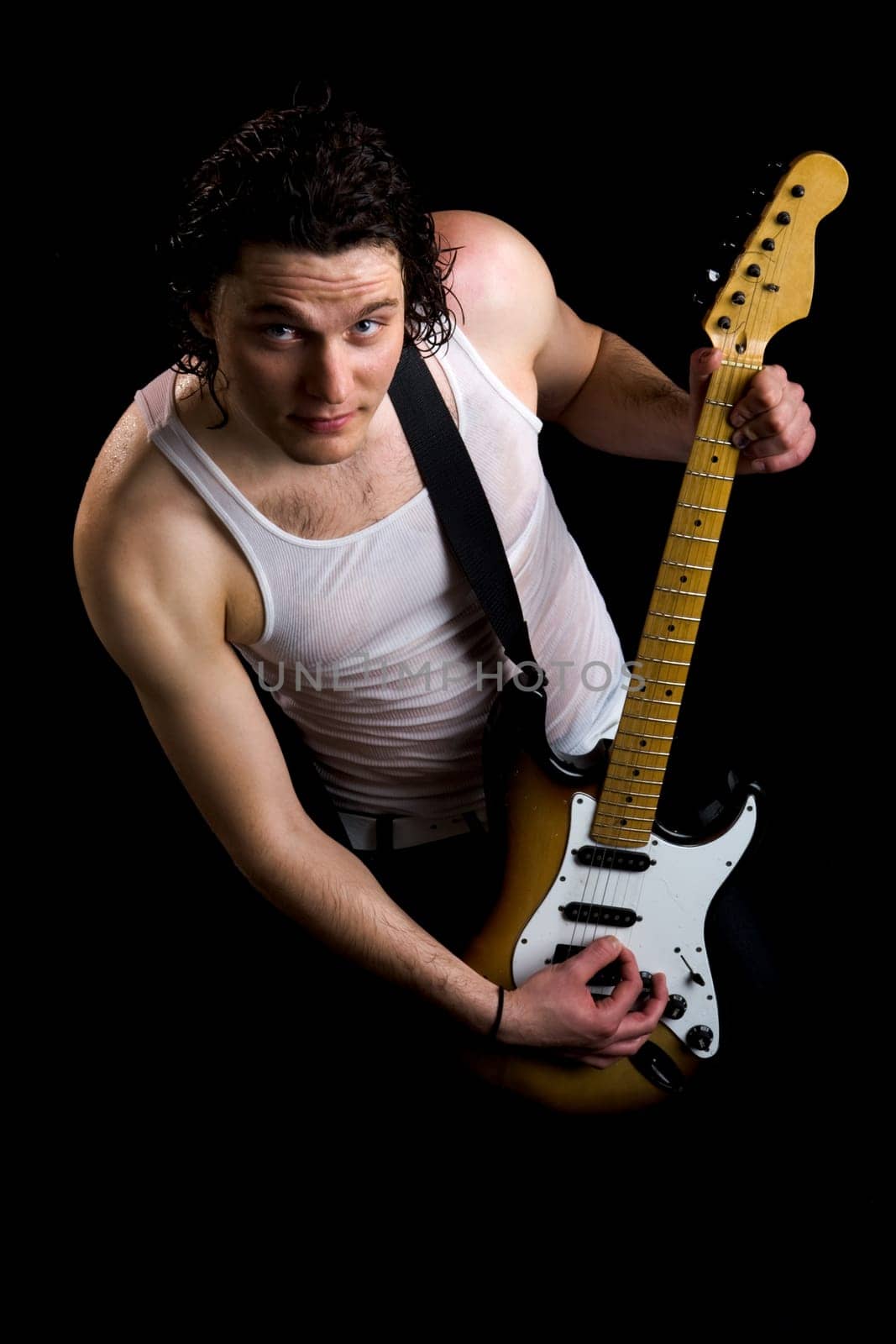 Portrait of guitar player in vest holding instrument over black background